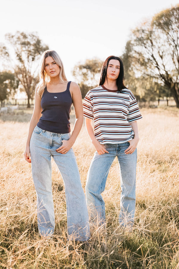 Woman wearing the Sadie Stripe Tee with light wash jeans, standing with another woman in a grassy paddock