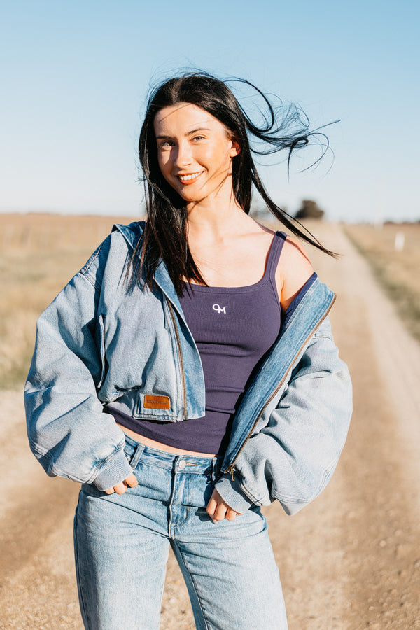 Woman wearing the Annie Denim Bomber open over a navy tank and jeans on a rural dirt road