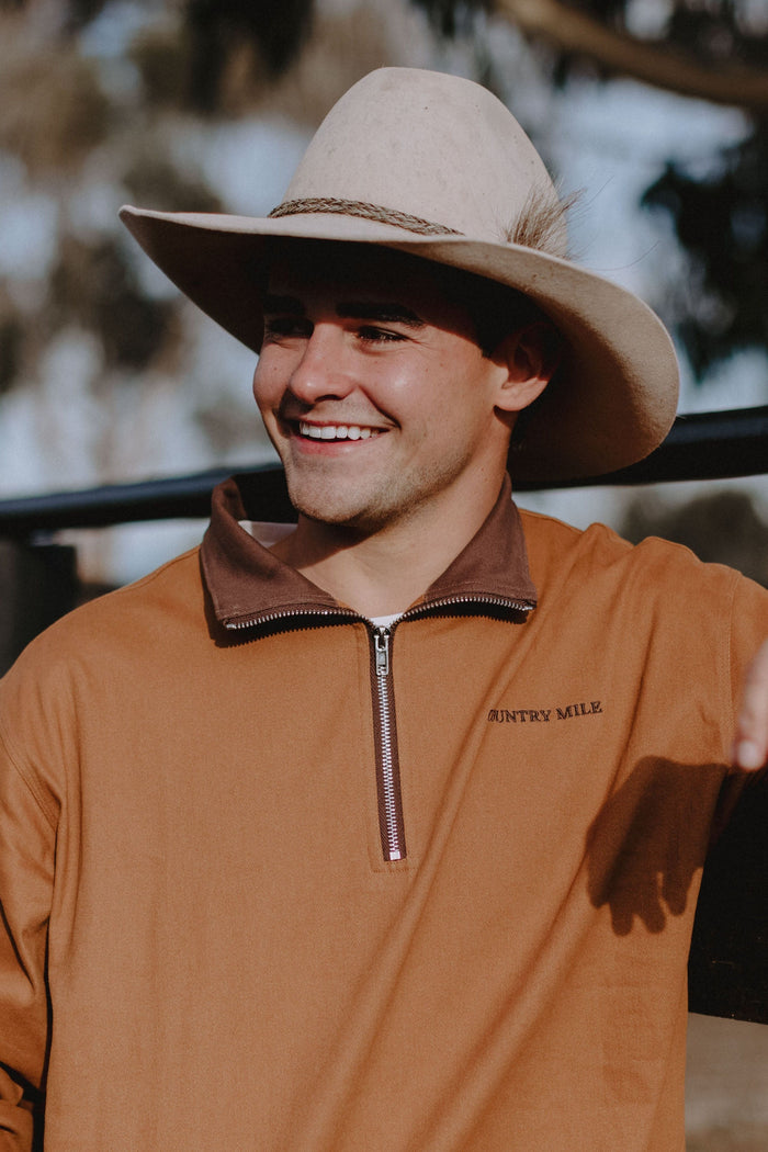 Man wearing the Macedon Pullover in rust with brown corduroy collar, white cowboy hat, laughing outdoors