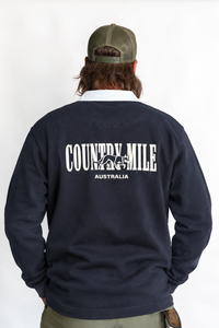 A man viewed from behind wearing a navy blue sweatshirt with a white graphic that reads 'COUNTRY MILE AUSTRALIA' on the back, along with an olive green cap and khaki pants, against a plain white background.