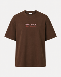 A brown short-sleeve crewneck t-shirt with 'GOOD LUCK' printed in white and 'bad luck' in red across the chest, displayed on a clean white background.