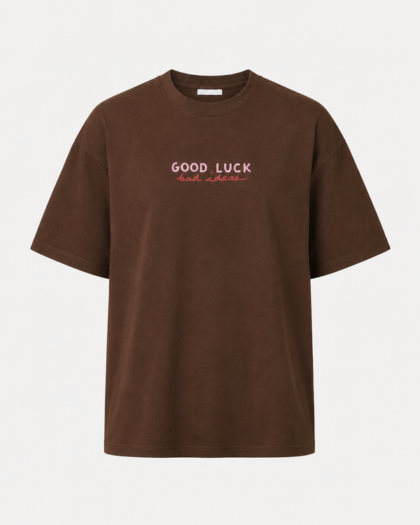 A brown short-sleeve crewneck t-shirt with 'GOOD LUCK' printed in white and 'bad luck' in red across the chest, displayed on a clean white background.