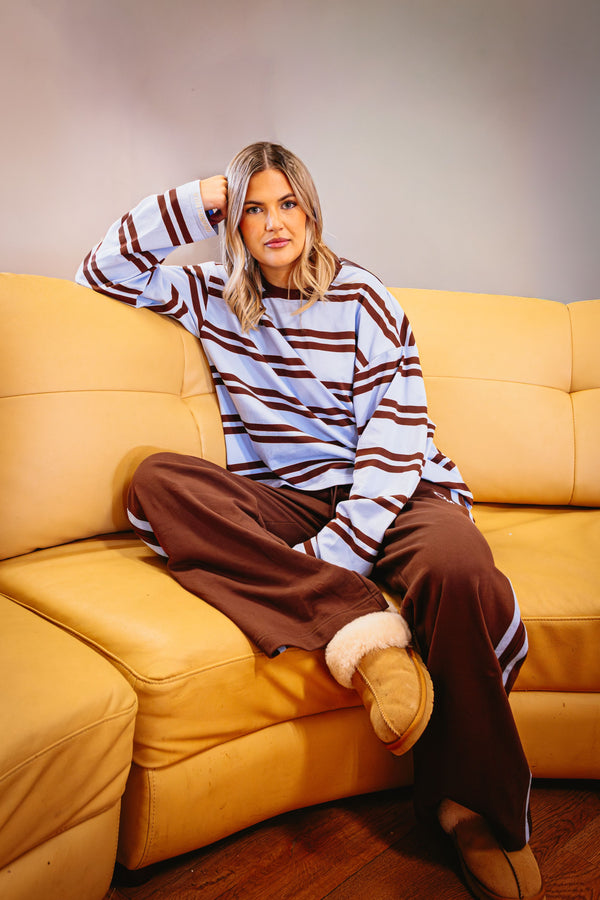 Woman sitting on a yellow couch wearing a striped sweater and brown pants.