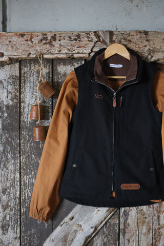 Macedon Pullover hanging on a hook, showing the black body, tan sleeves, corduroy collar and leather Country Mile patch