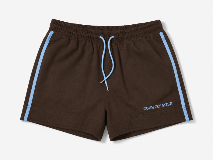 Dark brown work shorts with light blue side stripes, a matching light blue drawstring, and 'COUNTRY MILE' printed in light blue on the lower left leg, shown against a light gray background.