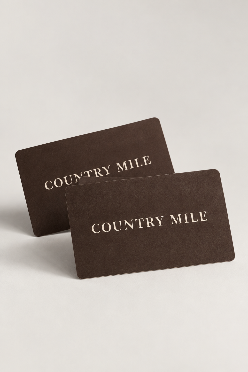 Two dark brown Country Mile gift cards with gold foil lettering, displayed on a light gray background.