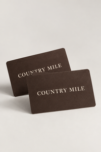 Two dark brown Country Mile gift cards with gold foil lettering, displayed on a light gray background.