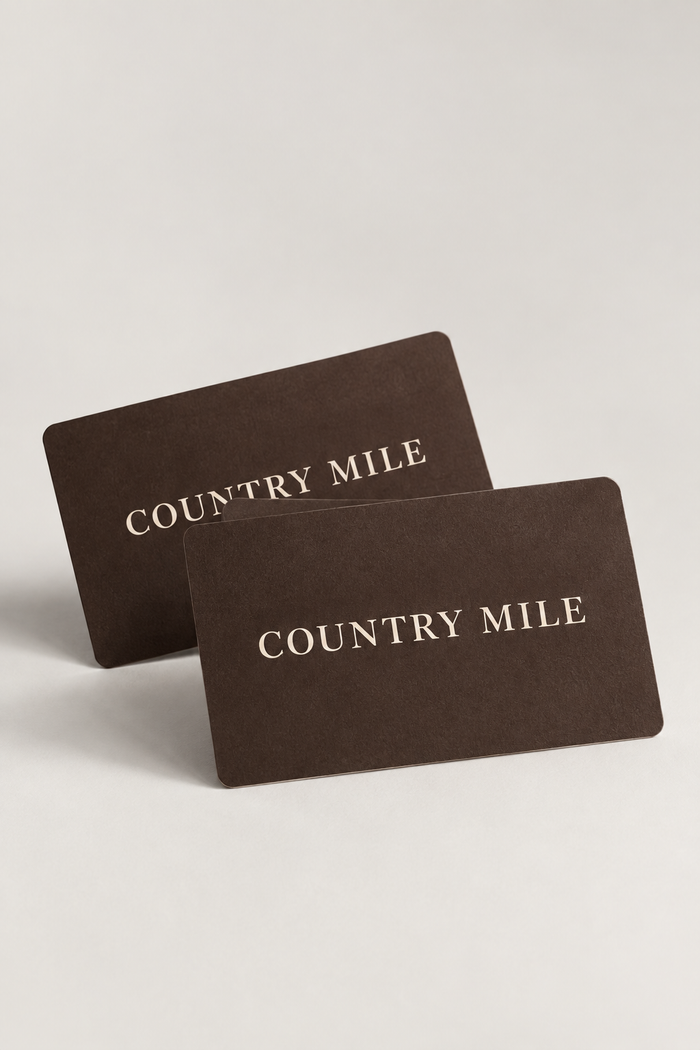 Two dark brown Country Mile gift cards with gold foil lettering, displayed on a light gray background.