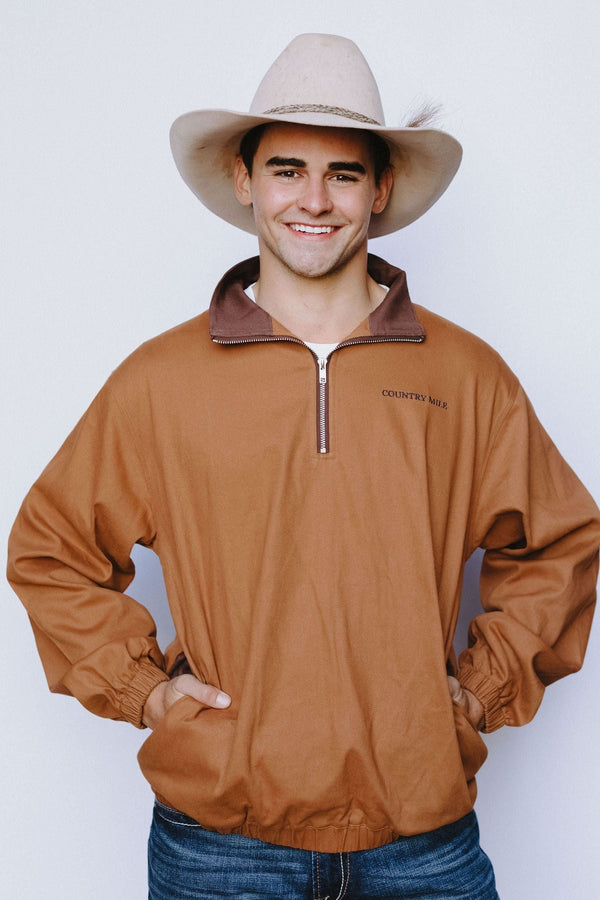 Man wearing the Macedon Pullover in rust with brown corduroy collar, white cowboy hat, hands in pockets